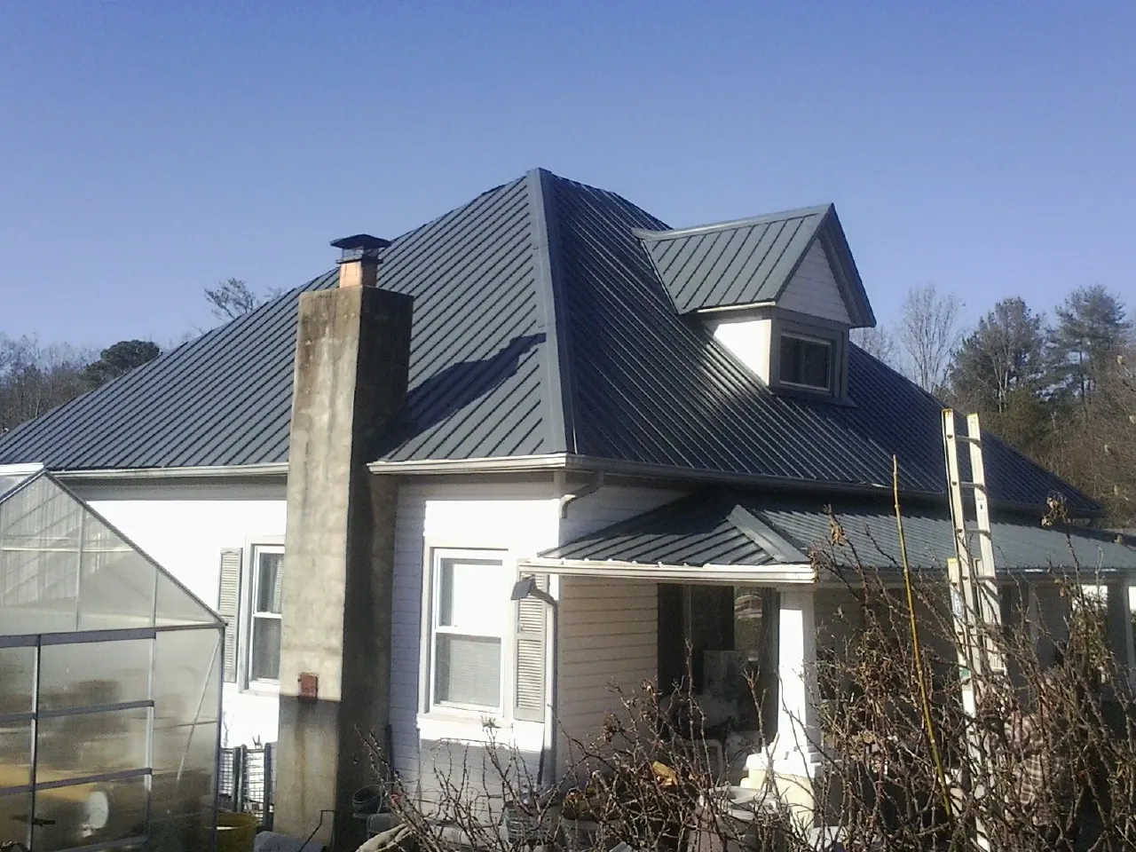 Dark blue standing seam metal roof on a white farmhouse with dormer — Slate & Tile Roof Repair by Roofing Brothers in Steamboat Springs