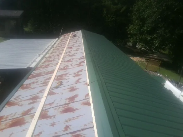 Old rusted panels beside newly installed green metal roofing — Wind Damage Roof Repair by Roofing Brothers in Steamboat Springs