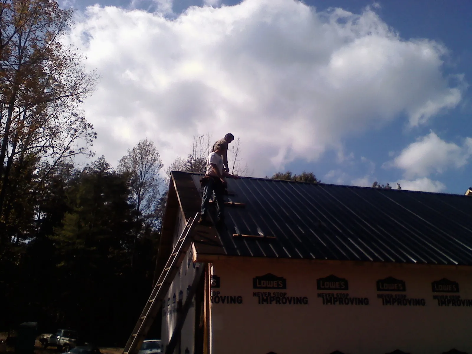 Roofer fastening dark metal panels high against a cloudy sky, from a Roof Inspection job in Steamboat Springs